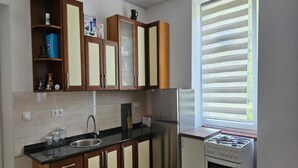 Una cucina compatta con mobili in legno, un frigorifero in acciaio inossidabile, un fornello a gas e una finestra con persiane.