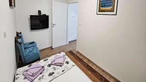 Una stanza piccola e pulita con un letto, una TV fissata al muro, una porta e una finestra con persiane.