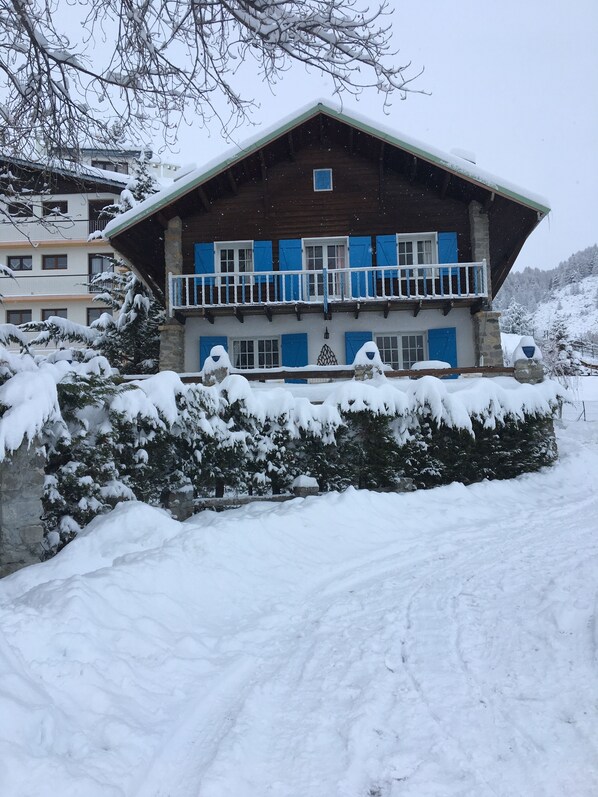 A two-story wooden building with blue shutters and a balcony, surrounded by snow-covered trees and a stone wall. - Auron Chalet Casanova Centre et Pistes à Pied (Saint-Étienne-de-Tinée)