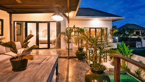 Un patio exterior moderno con una mesa de madera, plantas en macetas y vista a un edificio residencial.