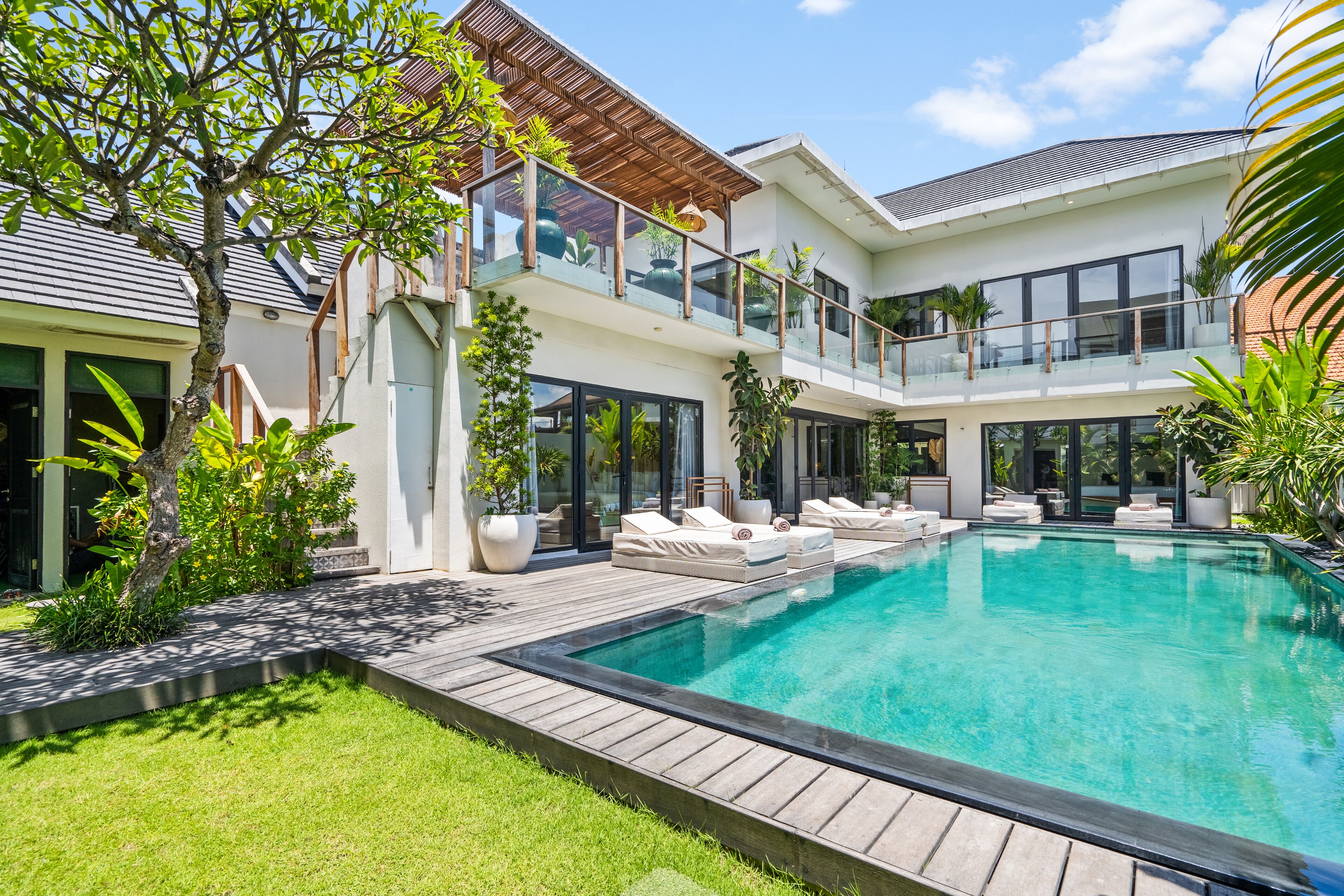 A modern house with a large swimming pool, multiple balconies, and lush greenery.