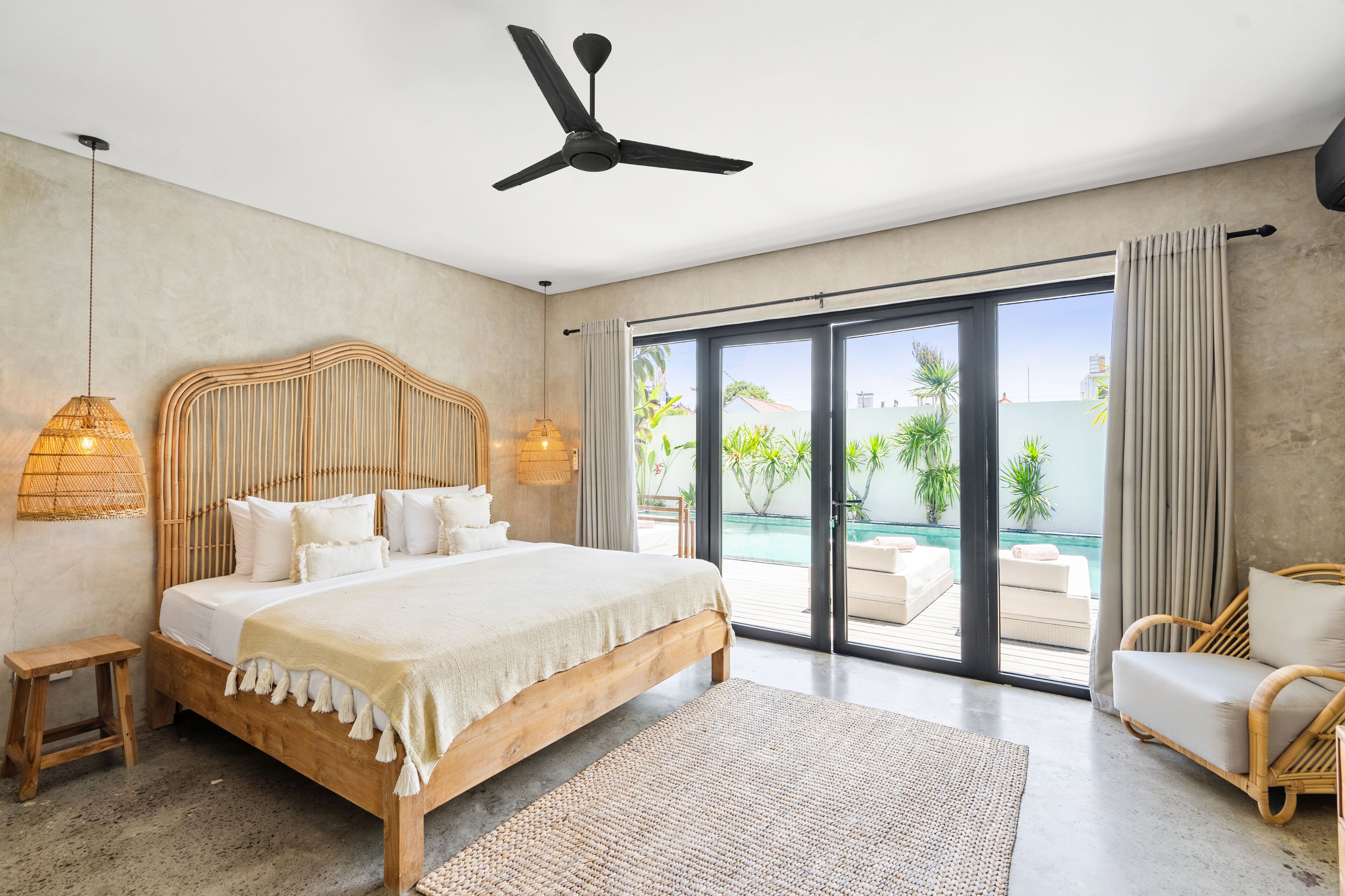 Un dormitorio moderno con una cama grande, ventilador de techo y vistas a una piscina y zonas verdes.