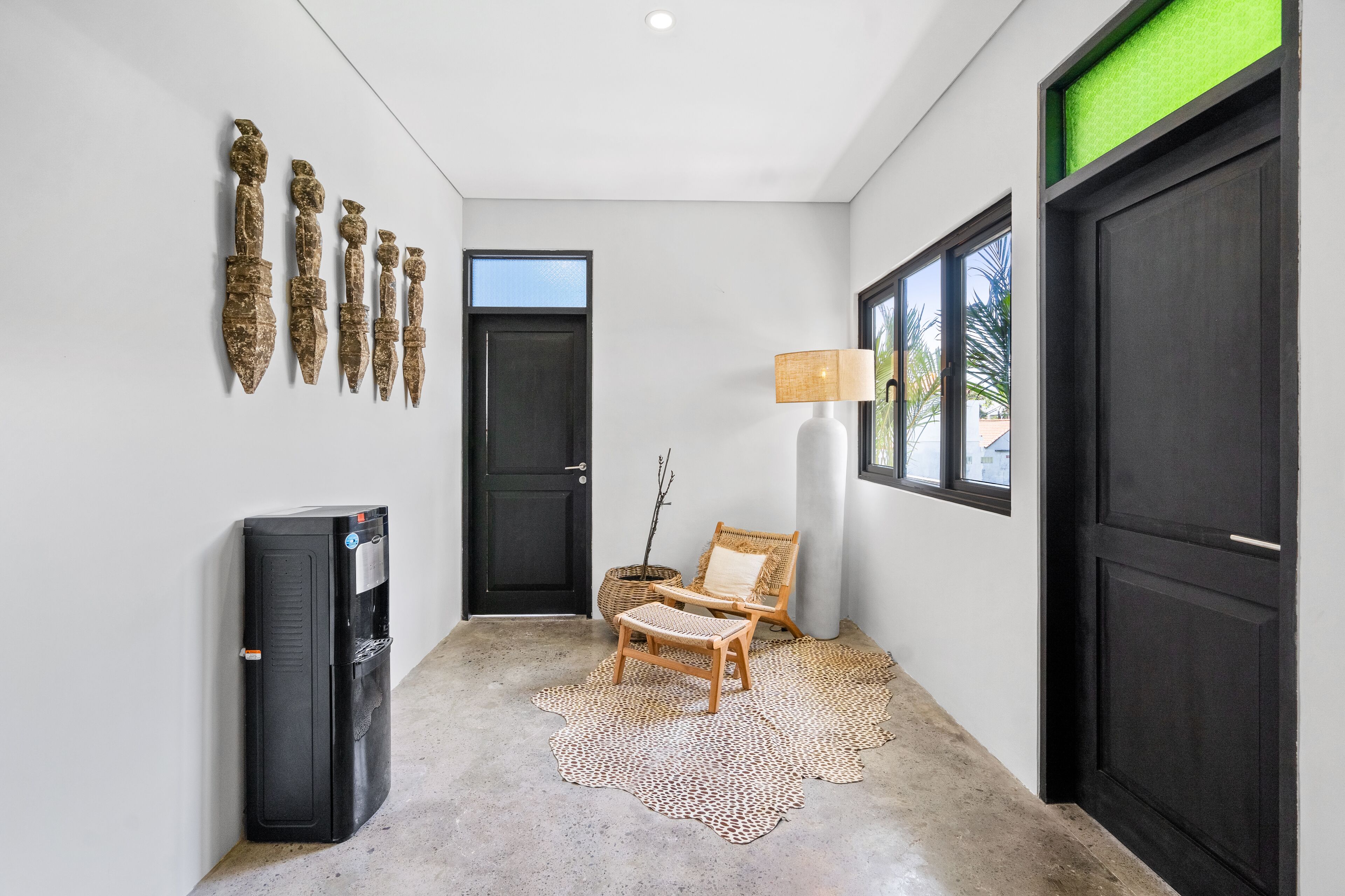 A hallway with a black refrigerator, a door, a chair, a lamp, and a patterned rug.