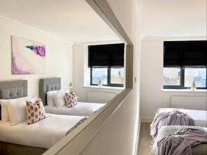 A hotel room with two beds, a large window with black blinds, a radiator, and a painting on the wall.