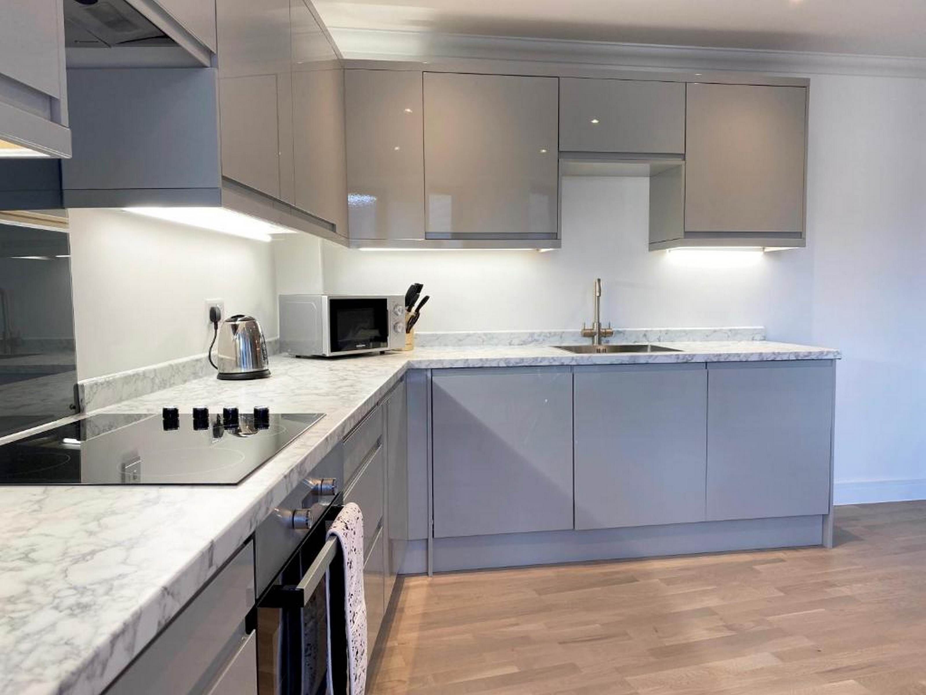 A modern kitchen with grey cabinets, a built-in oven, a microwave, and a sink.