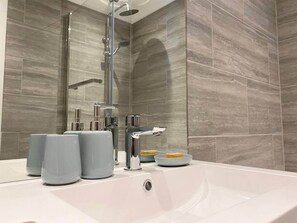 A modern bathroom with a white sink, chrome fixtures, and grey marble tiles.