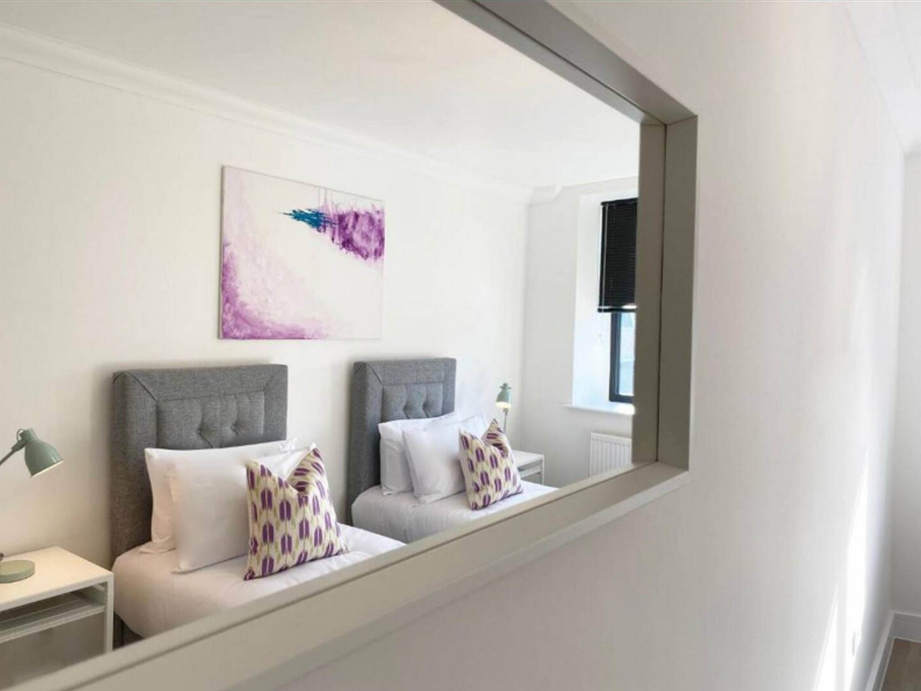 Un dormitorio moderno con dos camas, un espejo grande y un cuadro en la pared.