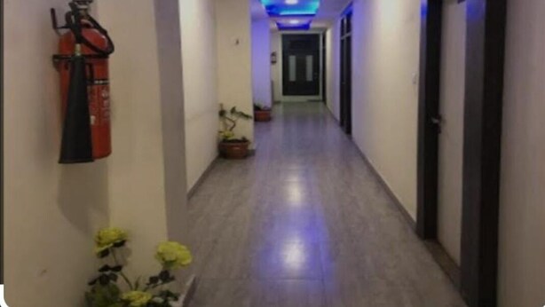 A hallway with a fire extinguisher mounted on the wall, potted plants, and a door at the end. - Hotel Nagpal (Haridwar)