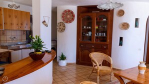 A kitchen with wooden cabinets, a sink, and a dining area with a chair and table. - La Casa di Margherita (Budoni)