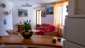 A cozy living room with a red sofa, a dining table with a bowl of fruit, and a refrigerator. - La Casa di Margherita (Budoni)