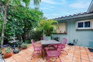 Eine Terrasse mit Tisch und Stühlen, umgeben von Pflanzgefäßen und einem kleinen Brunnen.