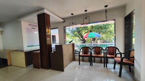 A reception area with a counter, chairs, and a view of the outdoors through a window. - Rain Raga Resort (Mahabaleshwar)