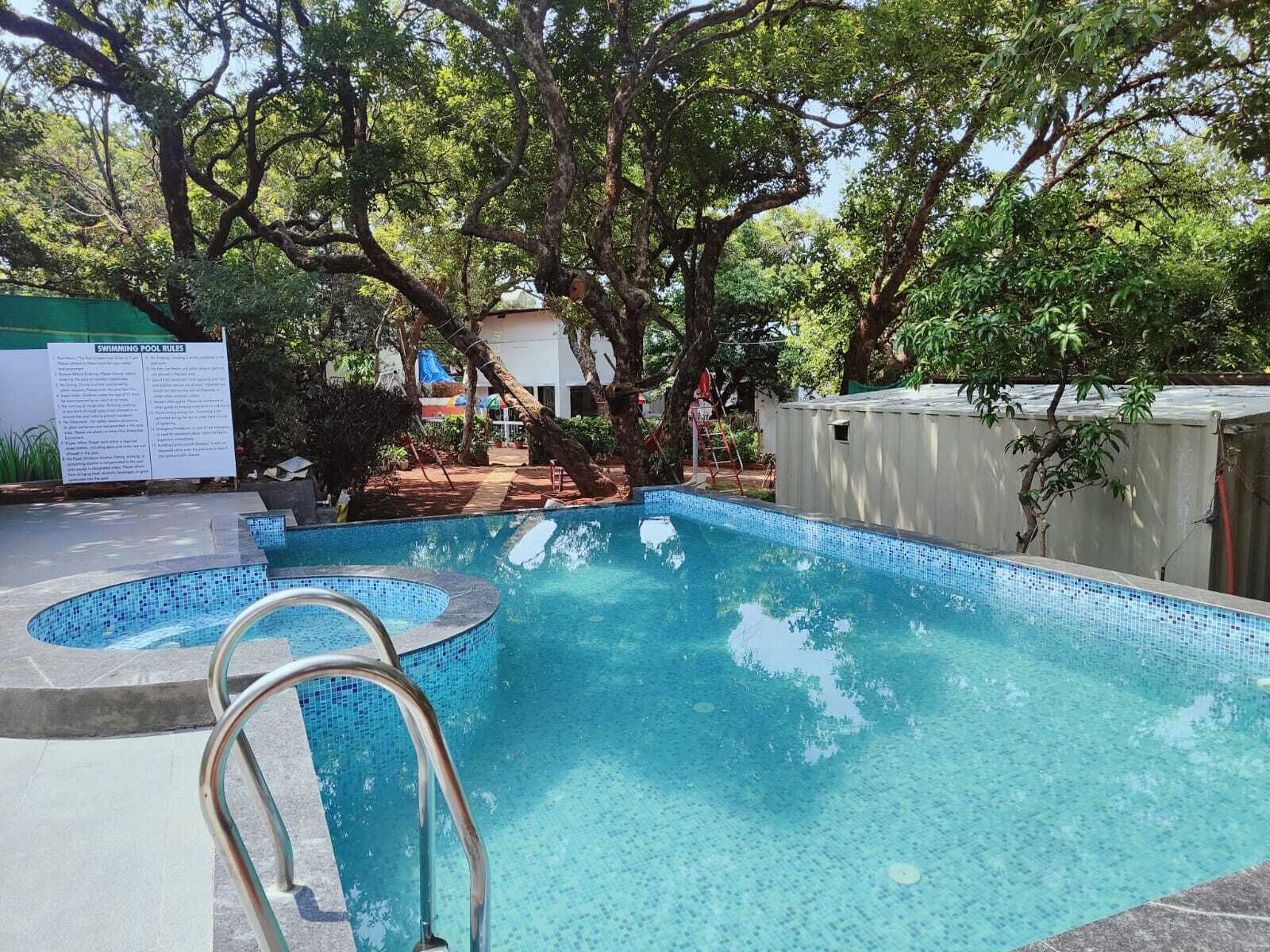 A swimming pool with a tiled edge, surrounded by trees and a covered area.
