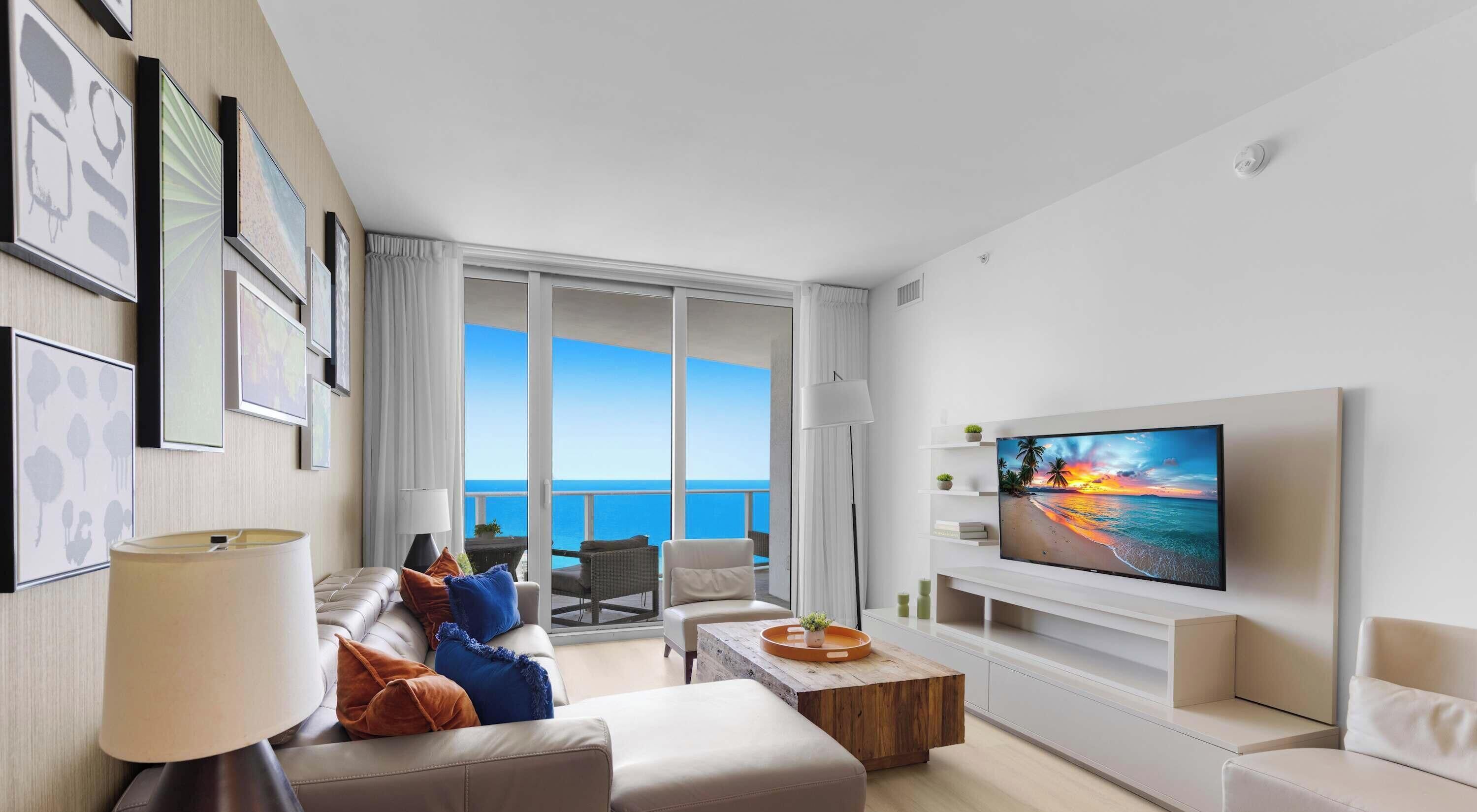 Una sala de estar moderna con un televisor grande, asientos cómodos y un balcón con vistas al mar.