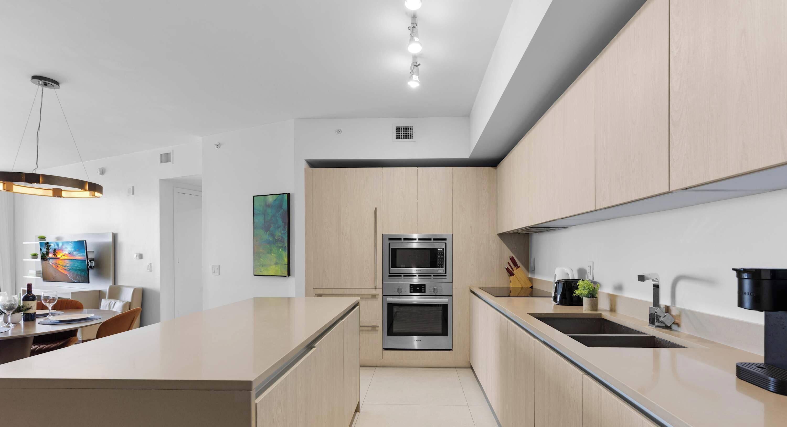 Een moderne keuken met een centraal eiland, roestvrijstalen apparatuur en licht houten kasten.