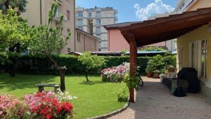 Un patio con una pérgola, un camino de grava y parterres de flores.