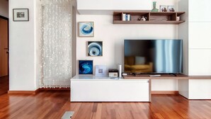 Una sala de estar moderna con un televisor de pantalla plana grande, piso de madera y un mueble blanco para entretenimiento con objetos decorativos.