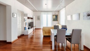 Una sala de estar moderna con comedor, piso de madera, sofá, televisor y obras de arte en las paredes.