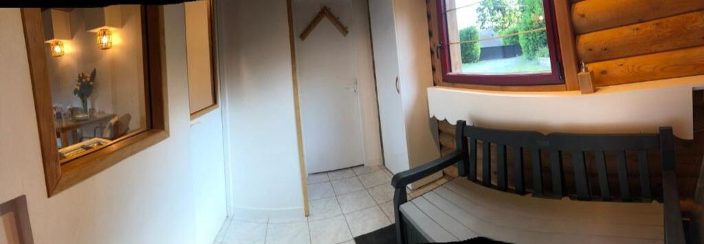 A room with a wooden bench, a window with a view of greenery, a mirror with wall-mounted lights, and a door.