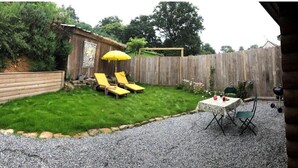 A backyard with a wooden fence, a gravel area, and a small patio with a table and chairs. - Neizhig Koad Petit Nid en Bois (Péaule)