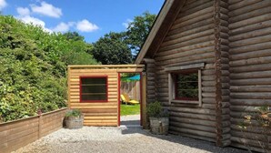 A log cabin with a small wooden structure attached, a gravel driveway, and a wooden fence. - Neizhig Koad Petit Nid en Bois (Péaule)