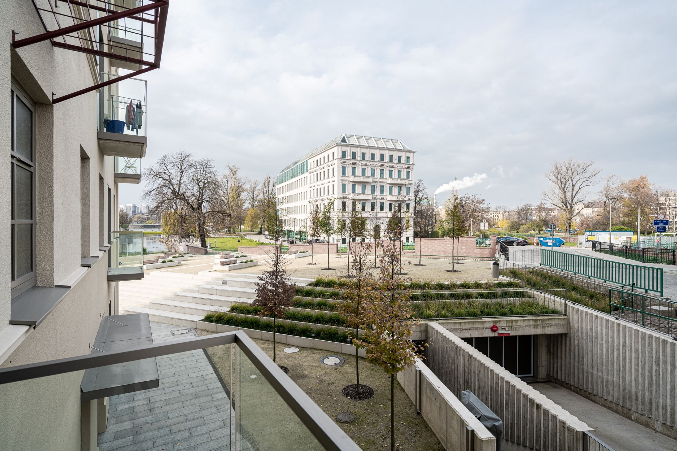 Un bâtiment moderne doté d’un balcon, d’une cour intérieure avec des arbres et d’un espace de stationnement.