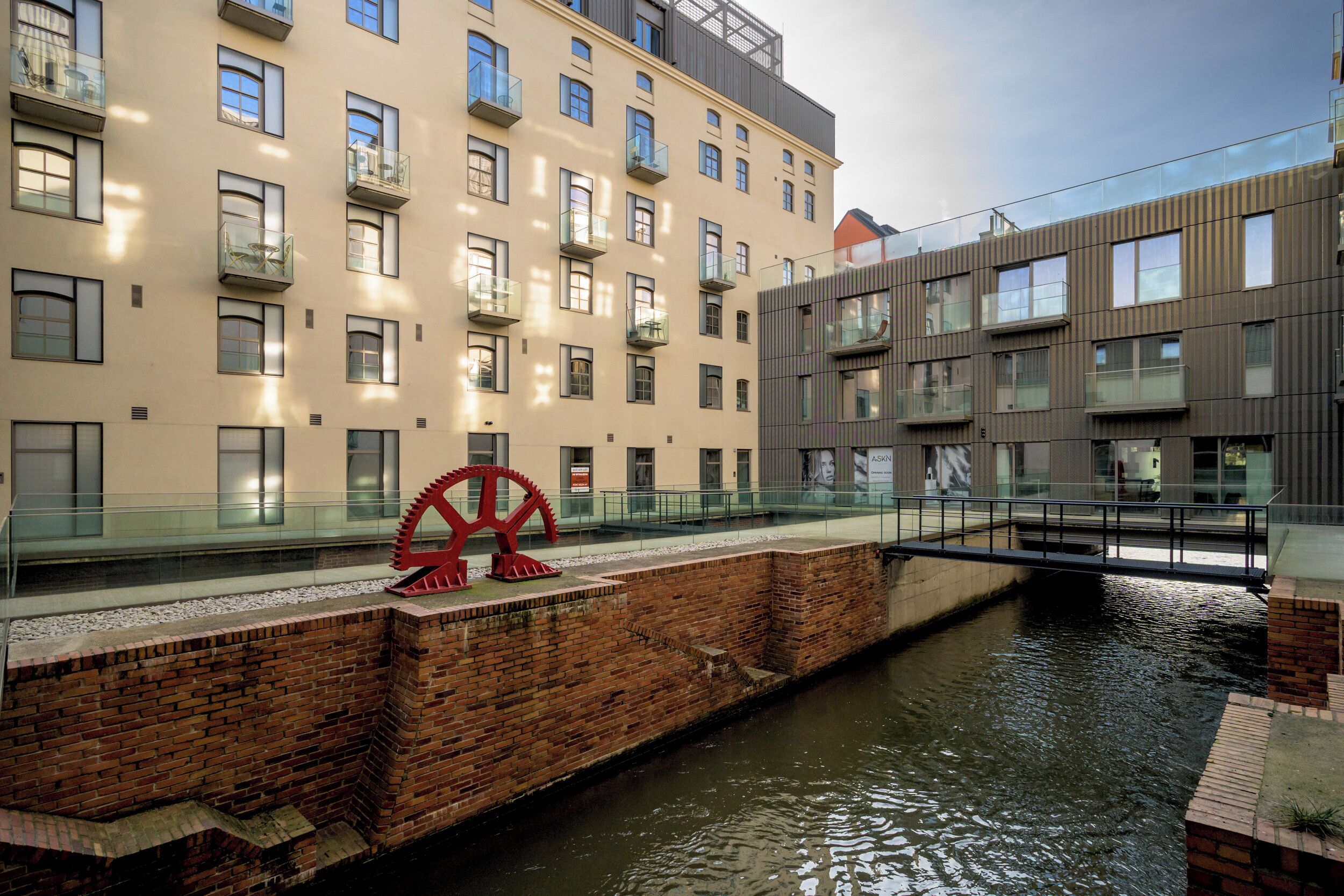 A modern building with multiple balconies, a red sculpture, and a canal.