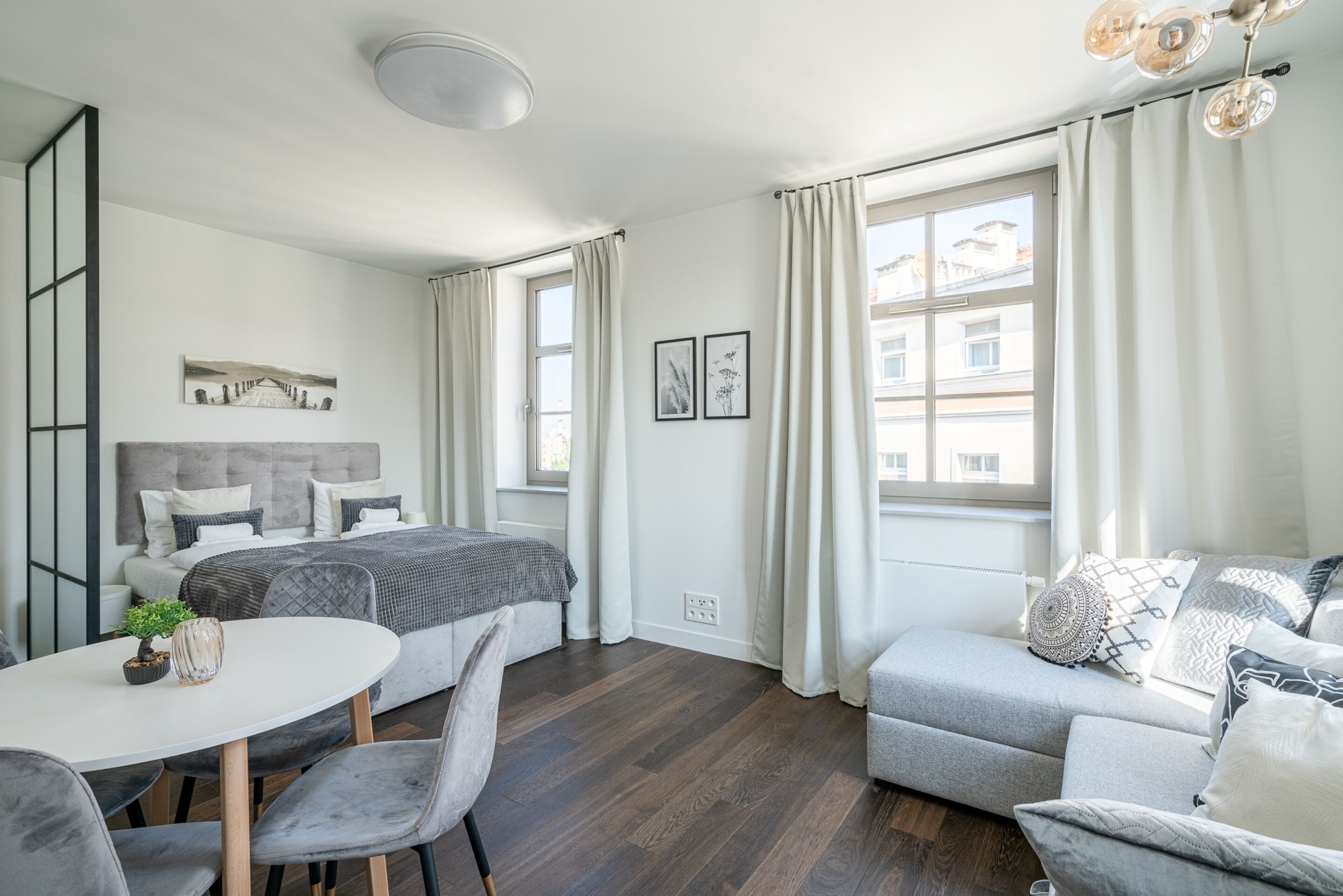 Una habitación moderna y bien iluminada con una cama, un sofá, una mesa de comedor y una planta pequeña.