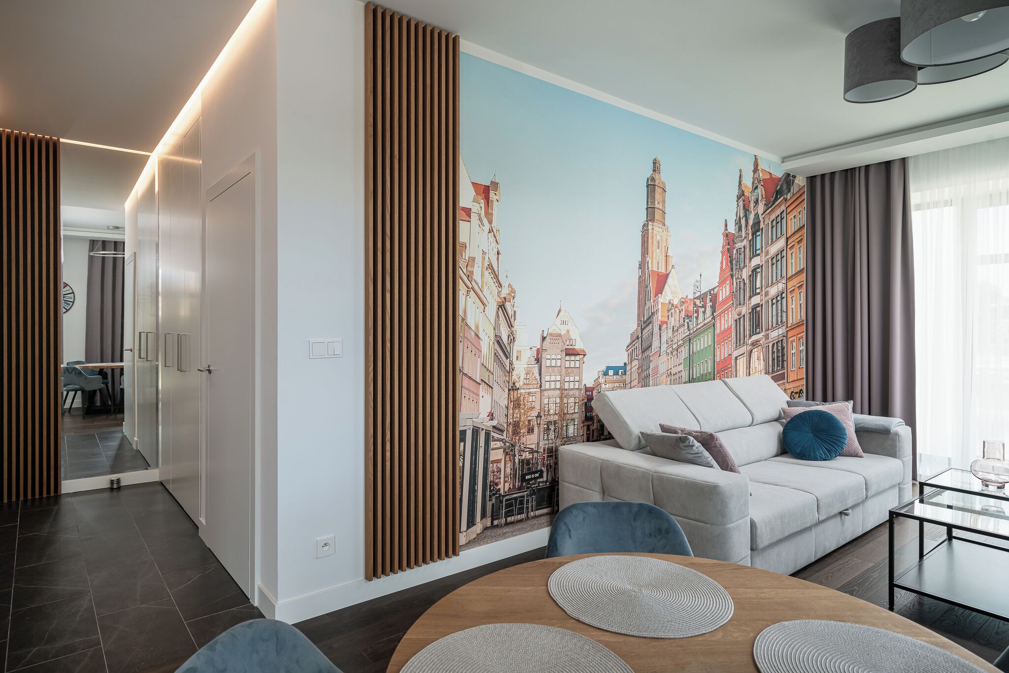 A modern living room with a cityscape mural, a sofa, a coffee table, and a dining area with a round table.