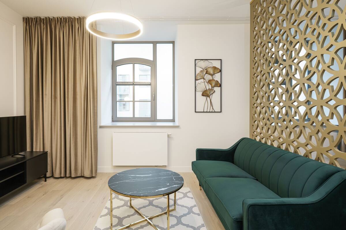 Uma sala de estar moderna com um sofá verde, uma mesa de centro preta e dourada, uma televisão e um painel decorativo na parede.