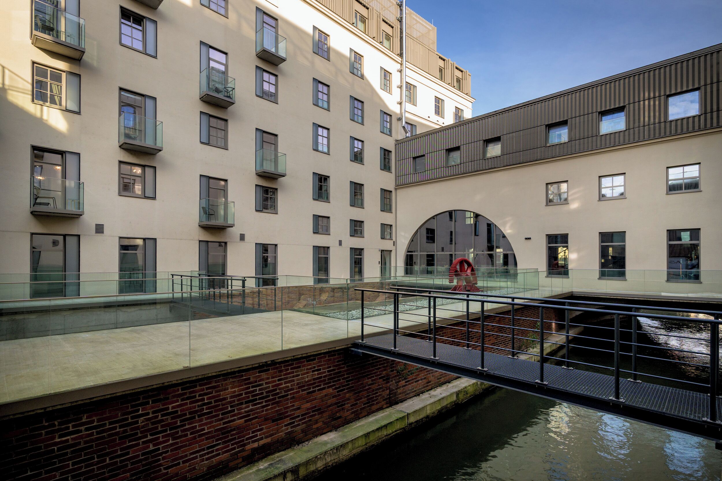 A modern building with multiple floors, large windows, and a glass bridge over a water channel.