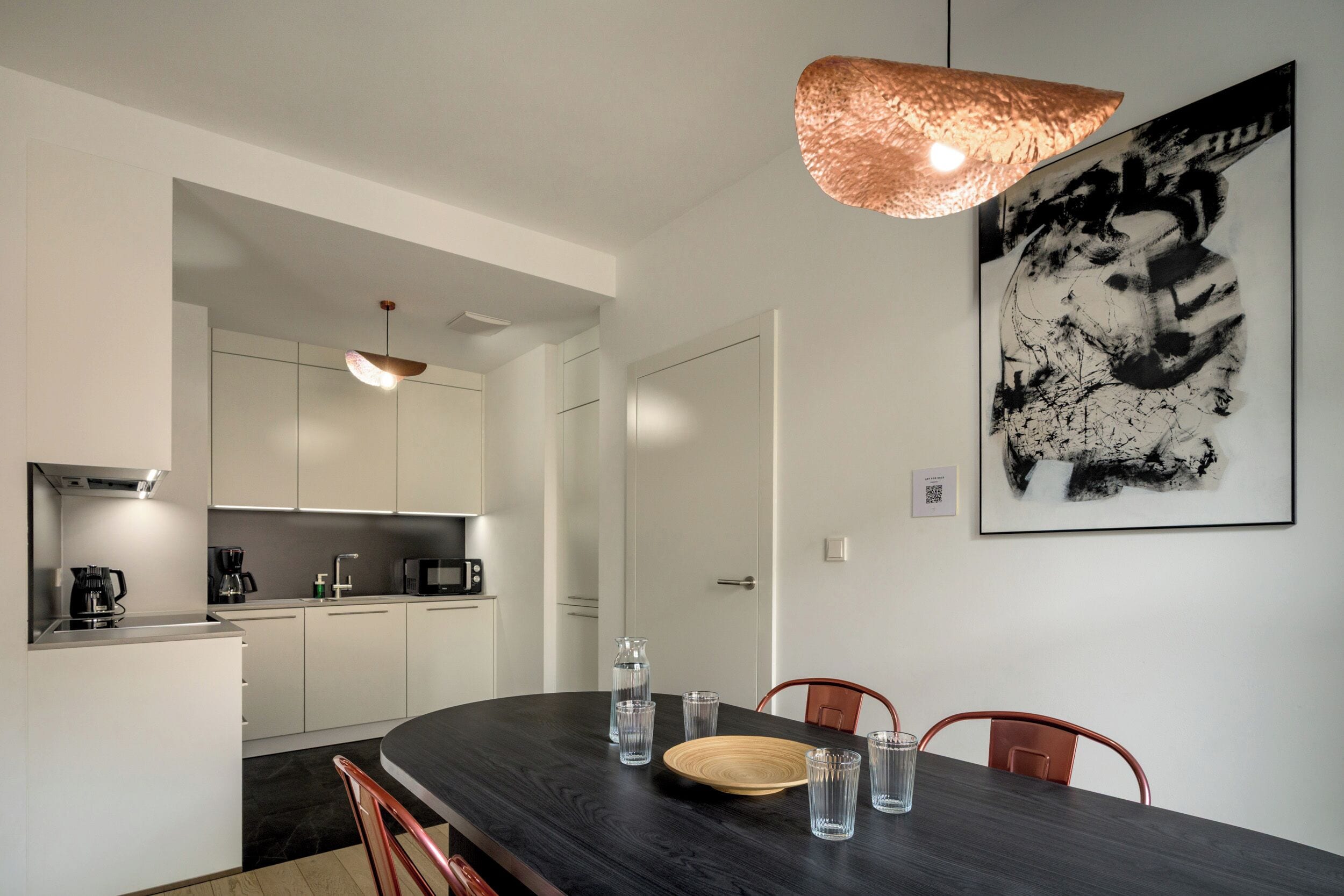 Una cocina moderna con armarios blancos, un comedor de madera oscura y un cuadro abstracto grande en la pared.