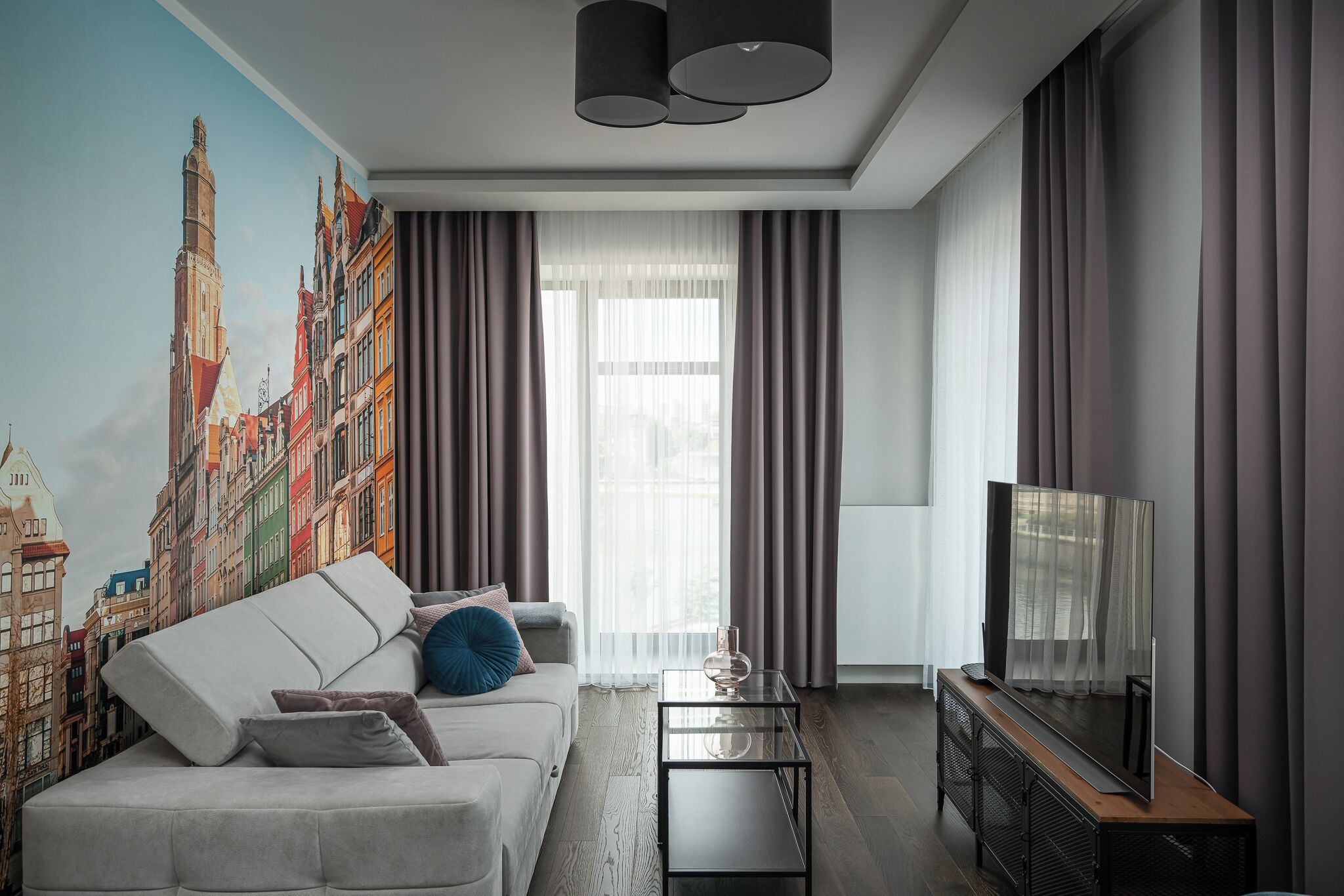 Un salon moderne avec une grande fresque représentant un paysage urbain, un canapé, une table basse et un téléviseur.