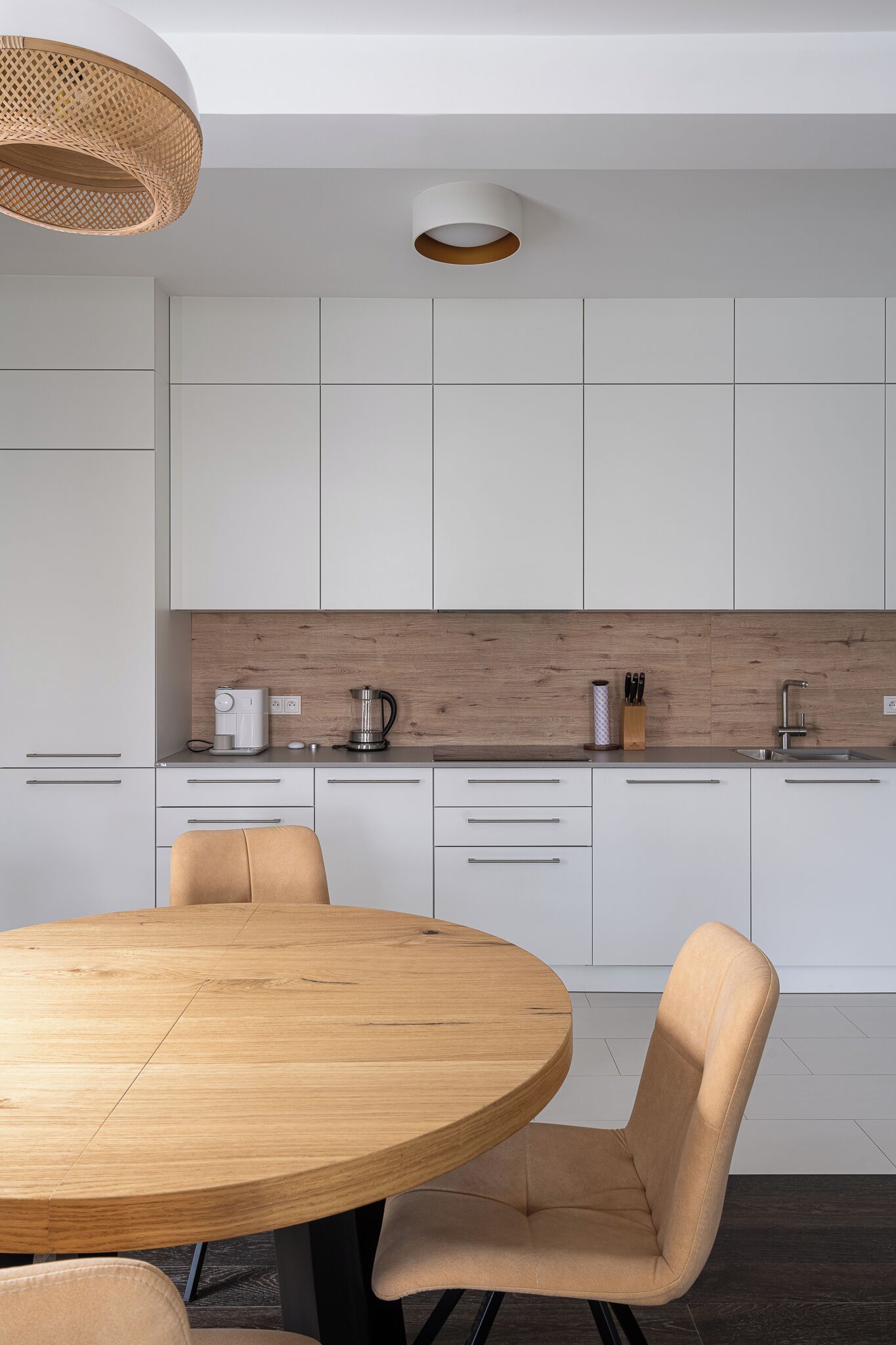 A modern kitchen with white cabinets, a wooden countertop, and a round wooden table with chairs.