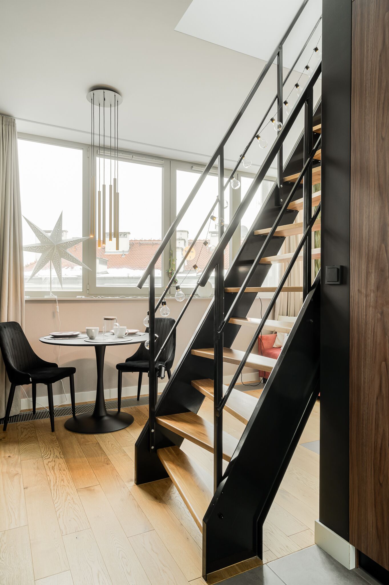 A modern interior with a staircase, a round table with chairs, and a large window with a star decoration.