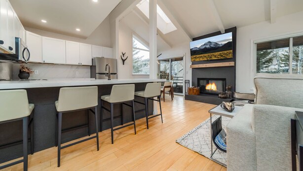 A modern kitchen with white cabinets, a stainless steel refrigerator, and a bar area with bar stools. - Beautifully Renovated 3BR, 3BA w Pool & Hot Tub (Snowmass Village)