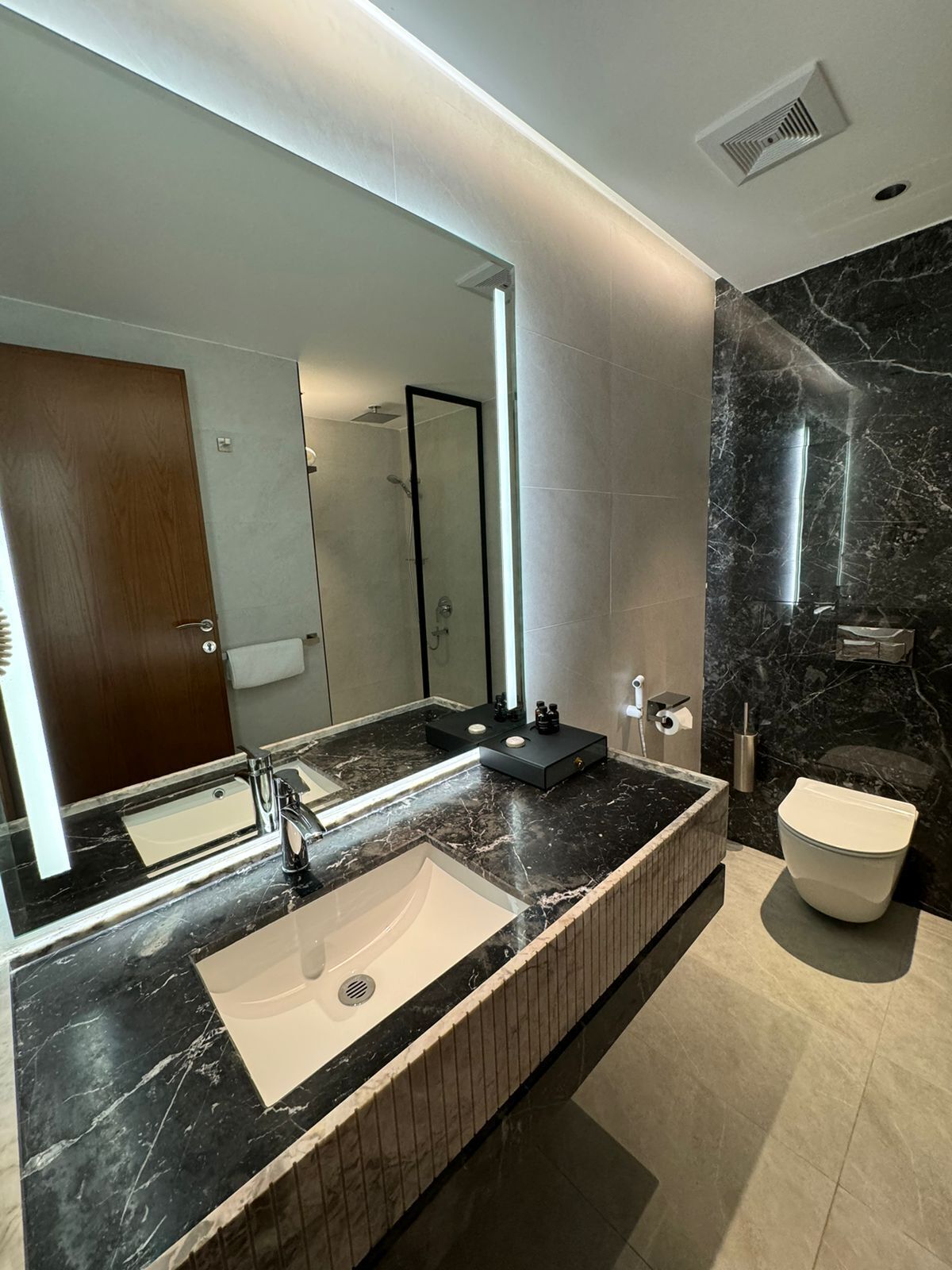 A modern bathroom with a large mirror, a bathtub, and a toilet.