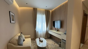 Une chambre d’hôtel moderne équipée d’un canapé, d’une petite table basse, d’un téléviseur à écran plat fixé au mur et d’une kitchenette compacte.