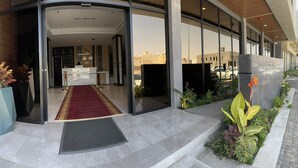 Une entrée d’hôtel moderne avec un comptoir d’accueil, un tapis rouge et une façade en verre.