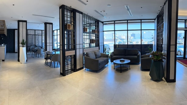 Un hall d’hôtel moderne comprenant un espace salon, un comptoir d’accueil et de grandes fenêtres donnant sur la ville.