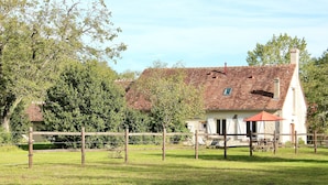 A rustic house with a red-tiled roof, surrounded by a wooden fence and lush greenery.