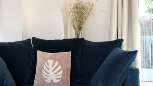 A dark blue sofa with a decorative pillow, a vase with dried flowers, and a window with curtains.
