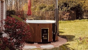 A hot tub in a garden with a wooden deck, surrounded by trees and a fence.