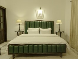 Una cama con cabecera tapizada en verde, dos lámparas de noche y un cuadro enmarcado sobre la cama.