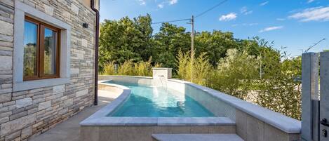 A swimming pool with steps leading up to it, surrounded by stone walls and greenery.