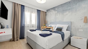 A modern hotel room with a large bed, a bedside table, a flat-screen TV, and a view of the city. - Casa Dika Pool & Lounge (Marcana)