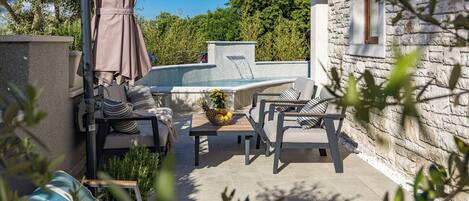 Ein Poolbereich mit Steinmauer, Gartenmöbeln und Blick auf die umliegende Grünfläche.