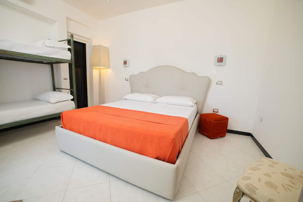A hotel room with a single bed, a bunk bed, a red ottoman, and a small table.