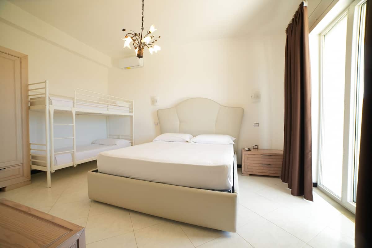 A bedroom with a large bed, a smaller bunk bed, a wooden nightstand, a dresser, and a window with curtains.