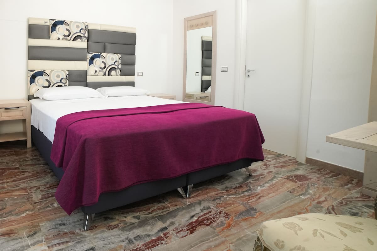 A modern bedroom with a bed, a nightstand, a dresser, a mirror, and a hanging light fixture.